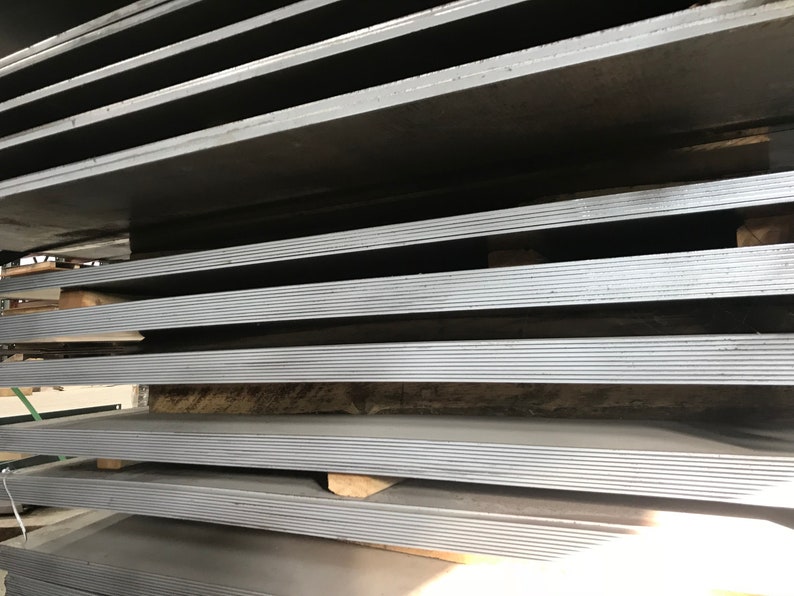 May include: A stack of gray metal sheets, likely steel, are stacked on top of each other. The sheets are arranged in a neat and organized manner, with each sheet slightly offset from the one below it. The sheets are all the same size and shape, and they appear to be new and unused.