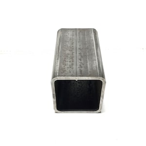 May include: A square metal tube with a rough, weathered surface. The tube is hollow and has a square opening at one end.