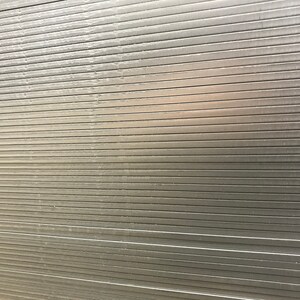 May include: A close-up of a silver metal surface with horizontal lines. The surface is smooth and reflective.