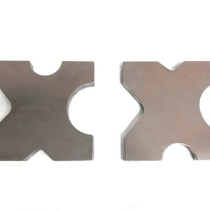 May include: Two metal pieces with a cross shape and a cut-out circle in the center of each arm. The pieces are a light brown color and have a rough texture.