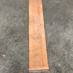 May include: A thin, rectangular piece of copper sheet metal. The metal has a slightly reddish-brown color and a textured surface.