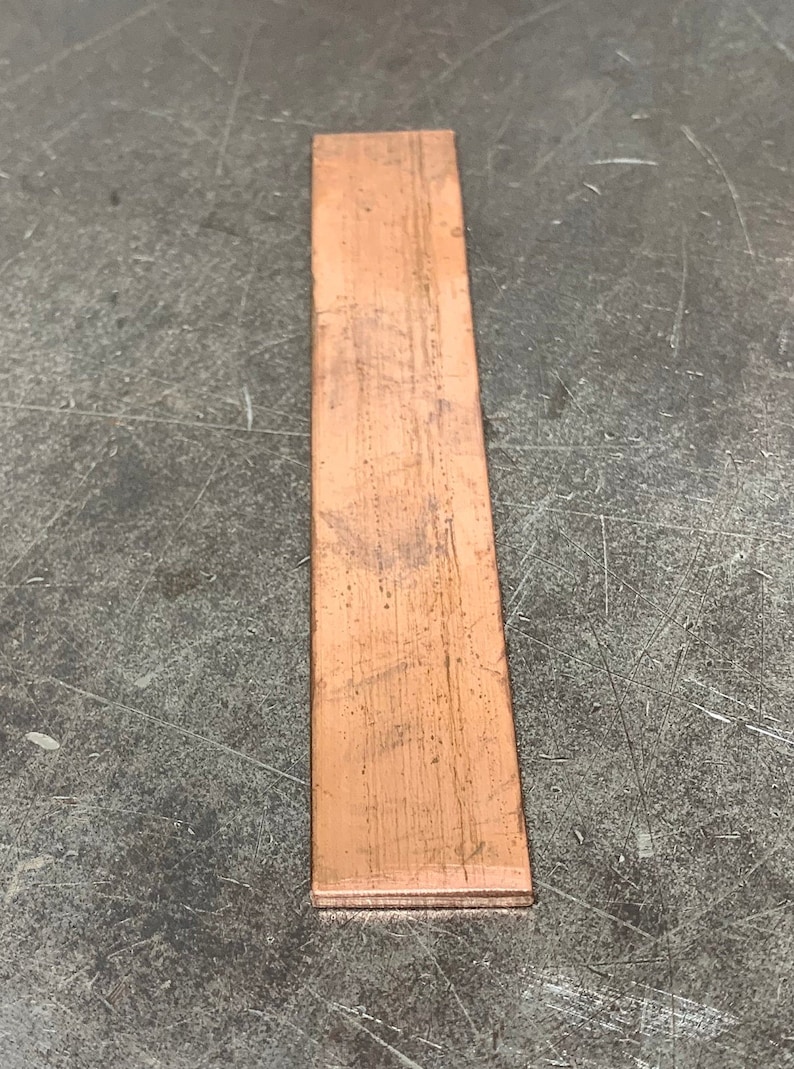 May include: A thin, rectangular piece of copper sheet metal. The metal has a slightly reddish-brown color and a textured surface.