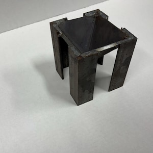 May include: A metal stand with a square base and four legs. The stand has a pyramid-shaped top.