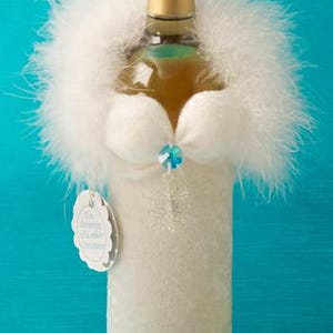 May include: A white wine bottle dressed in a white faux fur coat with a snowflake design and a blue rhinestone embellishment. The bottle has a tag that reads "It's beginning to look a lot like Christmas".