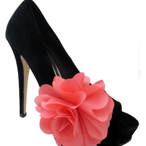 Puede incluir: Zapato negro de tacón alto con un gran adorno floral de color coral.