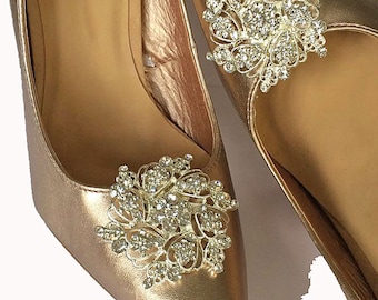 May include: A pair of gold shoes with a rhinestone embellishment on each toe.