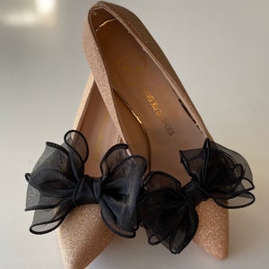 May include: A pair of gold glitter pointed-toe shoes with black tulle bows. The shoes have the text "DING XU'D SHOES" on the inside.