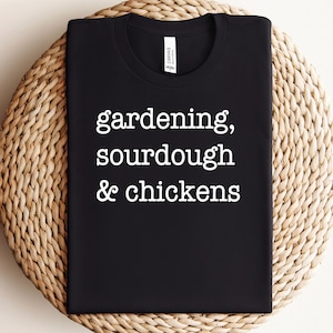 May include: Black t-shirt with white text that reads "gardening, sourdough & chickens".