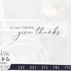May include: A white wooden cart with a wheel and the text "IN ALL THINGS give thanks" in black script. The cart is decorated with a floral arrangement. The text "Ivan & Co. DESIGNS" is in a black circle with a sunburst design. The text "SVG - DXF - EPS - PNG - PDF" is below the circle.