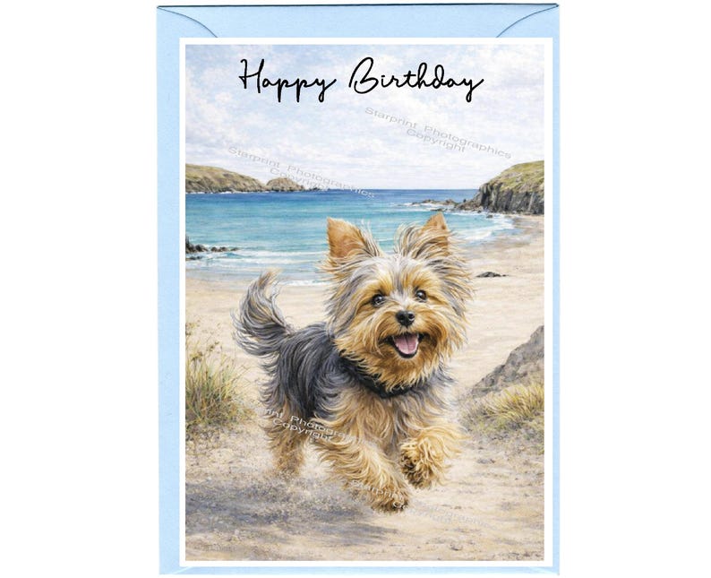 May include: A birthday greeting card featuring a Yorkshire Terrier running on a sandy beach with a blue ocean and sky in the background. The card has the words "Happy Birthday" written in black script.