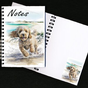 May include: A spiral bound notebook with a watercolor illustration of a brown and white dog running on a beach. The cover says "Notes".