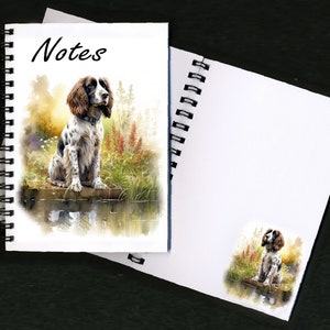 Può includere: Un quaderno a spirale con un'illustrazione ad acquerello di uno Springer Spaniel marrone e bianco seduto vicino a uno stagno. La copertina dice "Notes".