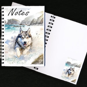 Könnte beinhalten: Spiralgebundenes Notizbuch mit einer Aquarellillustration eines Siberian Huskys, der am Strand läuft. Auf dem Cover steht das Wort "Notes". Das offene Notizbuch zeigt leere weiße Seiten.