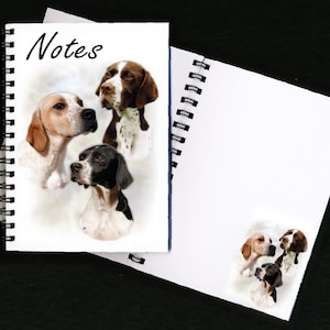 May include: Spiral-bound notebook with the word "Notes" in black script. The cover features watercolor portraits of three dogs: a brown and white dog, a brown and white spotted dog, and a black and white dog. A second notebook is partially visible.