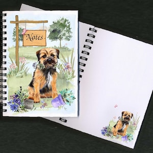 Può includere: Un quaderno a spirale con un'illustrazione ad acquerello di un Border Terrier seduto in un giardino. La copertina presenta un cartello che dice "Notes".