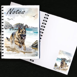 Puede incluir: Cuaderno de espiral con una ilustración en acuarela de un pastor alemán corriendo en una playa. La portada dice "Notes". El perro es marrón, negro y canela, con un fondo costero.