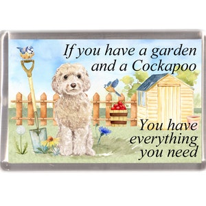 May include: A white Cockapoo dog sits in a garden with a wooden shed, a fence, a shovel, and a bucket of red apples. The text reads "If you have a garden and a Cockapoo, you have everything you need."