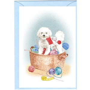 May include: A white dog with a red and white yarn ball in its mouth sits in a wicker basket filled with yarn balls and knitting needles.