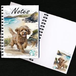 Può includere: Un quaderno a spirale con un'illustrazione ad acquerello di un cane marrone e bianco che corre su una spiaggia con una palla da spiaggia blu e verde. La copertina dice "Notes".