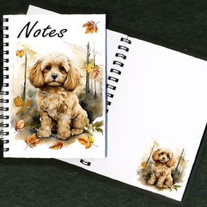 May include: A spiral bound notebook with a watercolor illustration of a small, light brown dog sitting in a forest setting with autumn leaves. The cover says "Notes" and the dog is looking directly at the viewer.