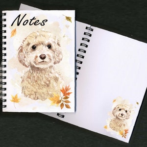 May include: A spiral bound notebook with a watercolor illustration of a white poodle on the front cover. The cover also features the word "Notes" and autumn leaves. The back cover is blank.