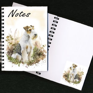 May include: A spiral bound notebook featuring a watercolour illustration of a wirehaired fox terrier sitting in a field of ferns. The front cover has the word "Notes" printed in black. The back cover features a smaller version of the dog illustration.