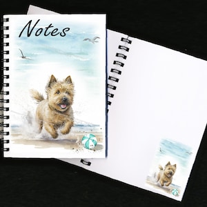Può includere: Quaderno a spirale con un'illustrazione ad acquerello di un cane che corre sulla spiaggia. La copertina ha la parola "Notes". Una piccola immagine del cane è sulla pagina interna. Lo sfondo presenta un cielo blu e gabbiani.