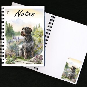May include: Spiral-bound notebook featuring a watercolour illustration of a dog by a lake. The cover displays the word "Notes". The dog is grey and brown, with a detailed depiction of the surrounding landscape.