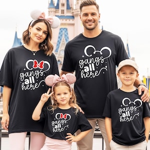 K&ouml;nnte beinhalten: Eine vierk&ouml;pfige Familie tr&auml;gt passende schwarze T-Shirts mit dem wei&szlig;en Text "gangs all here". Die Shirts zeigen ein Mickey Mouse-Kopf-Design. Der Hintergrund umfasst ein Schloss und andere Parkelemente.