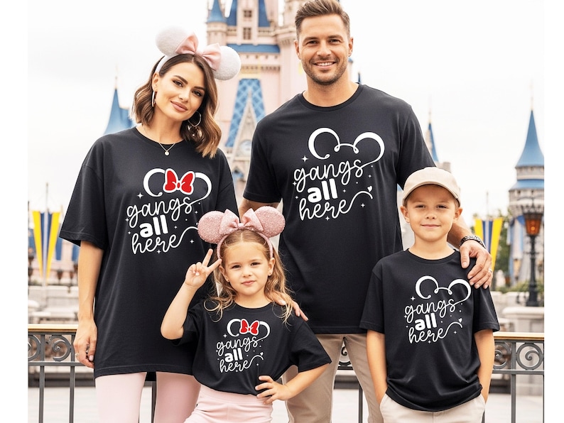 K&ouml;nnte beinhalten: Eine vierk&ouml;pfige Familie tr&auml;gt passende schwarze T-Shirts mit dem wei&szlig;en Text "gangs all here". Die Shirts zeigen ein Mickey Mouse-Kopf-Design. Der Hintergrund umfasst ein Schloss und andere Parkelemente.