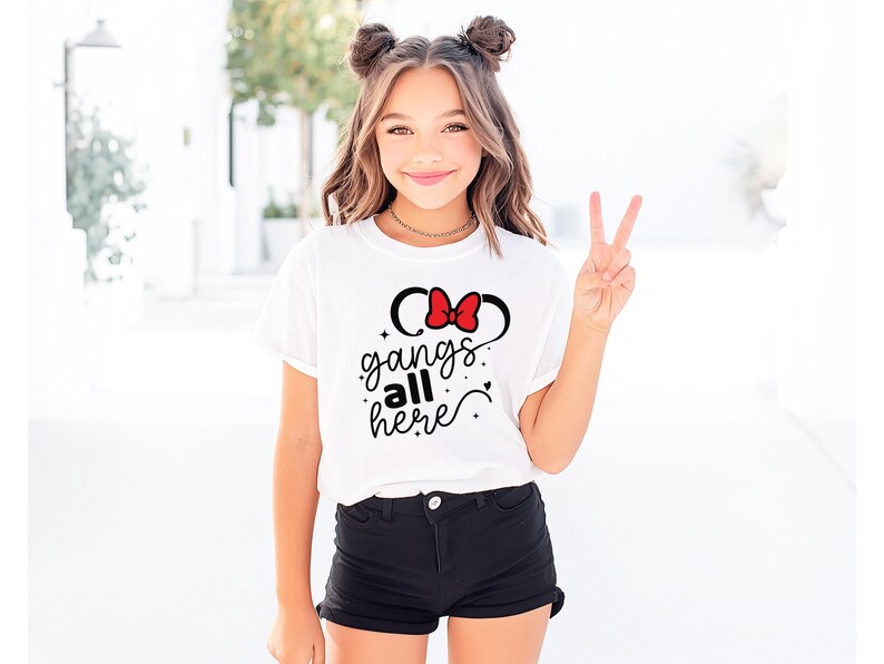 K&ouml;nnte beinhalten: Wei&szlig;es T-Shirt mit roter Schleife und schwarzem Mauseohren-Design sowie dem Text "gangs all here" in Schreibschrift. Das Shirt wird mit schwarzen Shorts kombiniert. Die Person, die das Shirt tr&auml;gt, zeigt das Victory-Zeichen.