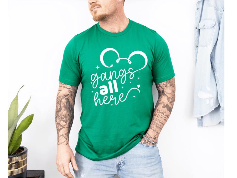 K&ouml;nnte beinhalten: Ein gr&uuml;nes T-Shirt mit wei&szlig;em Text, der "gangs all here" lautet. Das Design enth&auml;lt eine Mickey Mouse-Ohrenform &uuml;ber dem Text. Das Shirt hat eine einfarbige gr&uuml;ne Farbe.