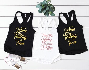 May include: Three tank tops with gold lettering. Two black tank tops say "Wine Tasting Team". One white tank top says "Pour the Wine HISLASTNAME is Mine" in gold and pink lettering.