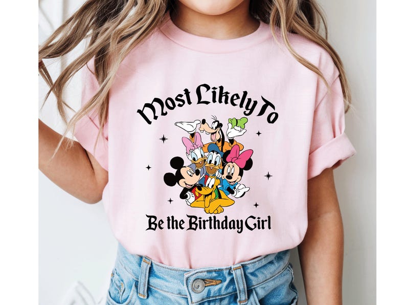 May include: A light pink t-shirt featuring a graphic of Disney characters including Mickey Mouse, Minnie Mouse, Donald Duck, Daisy Duck, Goofy, and Pluto. The text "Most Likely To Be the Birthday Girl" is printed above and below the characters.