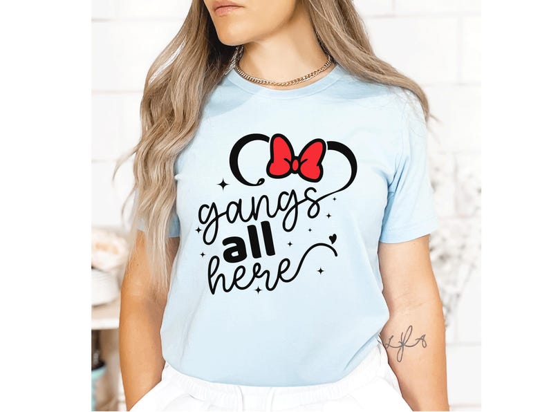 K&ouml;nnte beinhalten: Hellblaues T-Shirt mit einem Minnie-Mouse-inspirierten Design. Das Design zeigt schwarze Micky-Maus-Ohren mit einer roten Schleife und den Schriftzug "gangs all here" in einer verspielten Schriftart. Ein l&auml;ssiges Kleidungsst&uuml;ck.