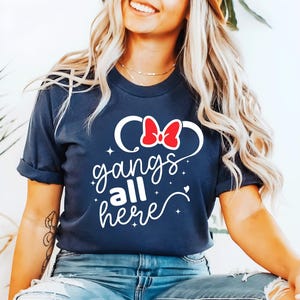 K&ouml;nnte beinhalten: Marineblaues T-Shirt mit dem wei&szlig;en Schriftzug "gangs all here". Das Design beinhaltet eine rote Schleife und wei&szlig;e Mickey Mouse Ohren. Ein l&auml;ssiges T-Shirt.
