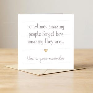 Op de afbeelding: Een witte wenskaart met de tekst "sometimes amazing people forget how amazing they are..." en "this is your reminder" in een handschriftstijl. Een klein gouden hartje staat onder de tekst. De kaart ligt op een bruine envelop.