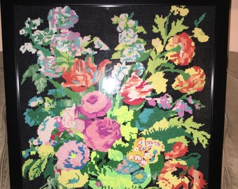May include: A framed needlepoint artwork depicting a colourful floral arrangement in a green vase against a black background.