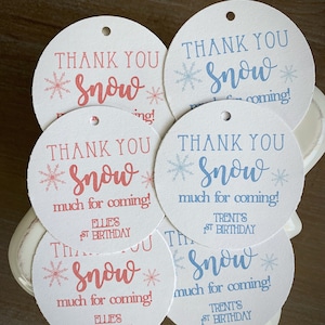 May include: Six round white thank you tags with a snowflake design and the text "Thank You Snow" in blue and pink. The tags are for a first birthday party and include the names "Ellie's" and "Trent's".