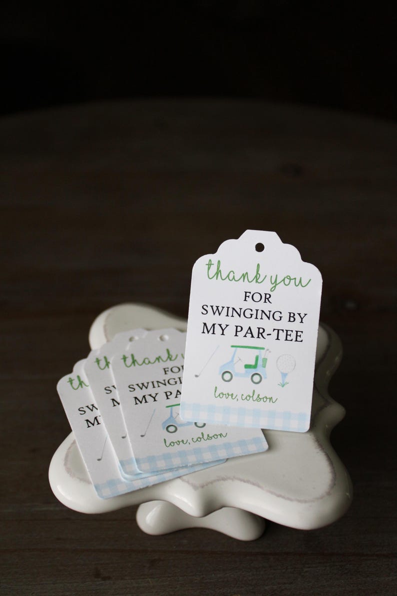 May include: A stack of white thank you tags with blue and white checkered pattern on the bottom. The tags have green text that says "thank you for swinging by my par-tee" with a cartoon golf cart and golf ball. The text "love, colson" is printed on the bottom of the tag.