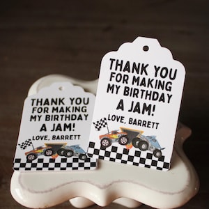 May include: Two white gift tags with a scalloped top edge. Each tag has the text "THANK YOU FOR MAKING MY BIRTHDAY A JAM! LOVE, BARRETT" in black. The tags feature illustrations of race cars and checkered flags.