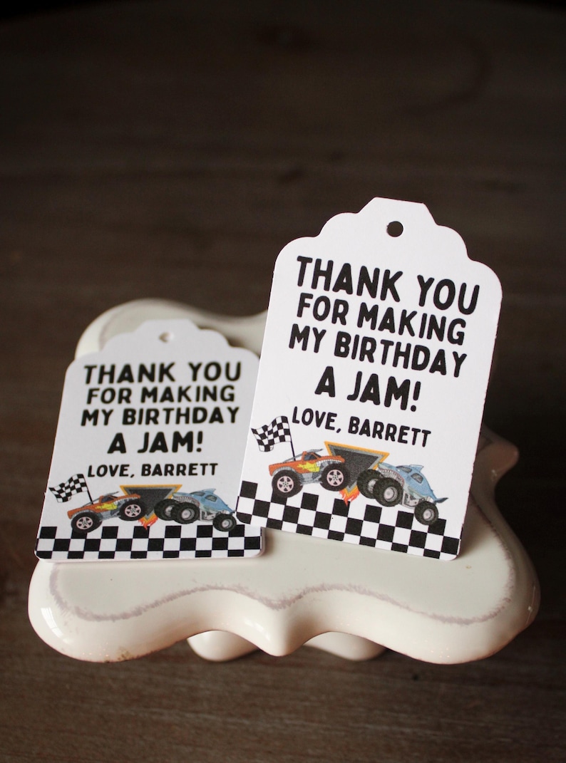 May include: Two white gift tags with a scalloped top edge. Each tag has the text "THANK YOU FOR MAKING MY BIRTHDAY A JAM! LOVE, BARRETT" in black. The tags feature illustrations of race cars and checkered flags.