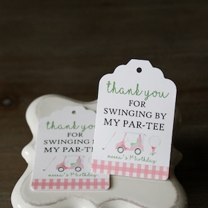 May include: Two pink and white thank you tags with a golf cart and golf ball design. The text on the tags reads "Thank you for swinging by my par-tee".