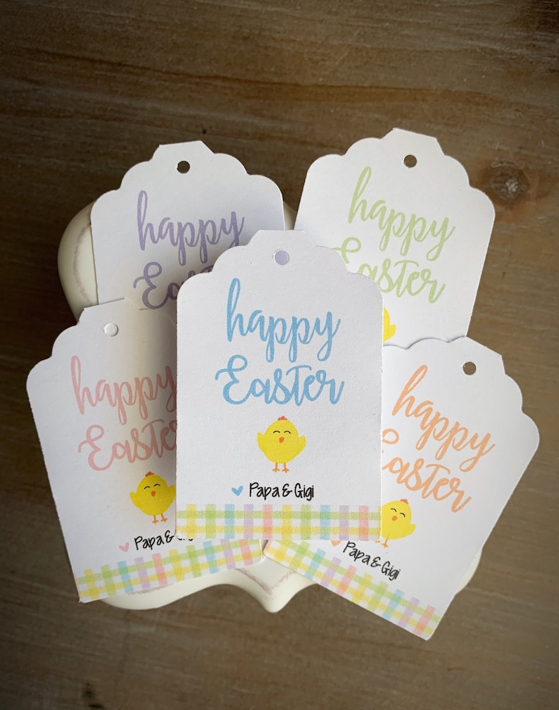 Puede incluir: Cinco etiquetas de regalo blancas con bordes festoneados y un agujero perforado en la parte superior. Cada etiqueta presenta una ilustraci&oacute;n de un pollito amarillo y el texto "happy Easter" en una fuente de letra cursiva colorida. Las etiquetas tienen un borde a cuadros en colores pastel y el texto "Papa & Gigi" en la parte inferior.