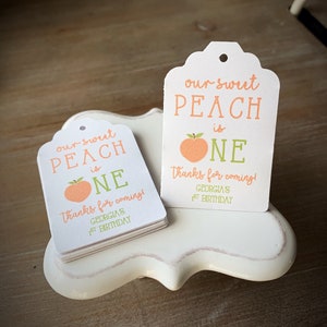 May include: Peach-themed favor tags with the text "our sweet peach is one" and "thanks for coming! Georgia's 1st birthday".