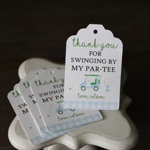 May include: White thank you tags with green text that reads "Thank you for swinging by my par-tee". The tags feature a cartoon golf cart and golf ball. The bottom of the tag has a blue and white gingham pattern and the text "love, colson".