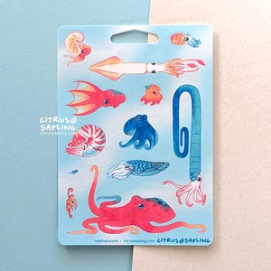 May include: A sticker sheet featuring watercolor illustrations of various cephalopods, including squid, octopus, and nautilus. The designs are in shades of red, orange, blue, and white, set against a light blue background. The text "CITRUS SAPLING" and website address are visible.