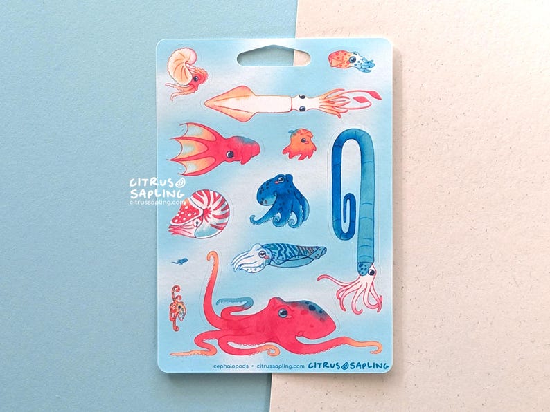 May include: A sticker sheet featuring watercolor illustrations of various cephalopods, including squid, octopus, and nautilus. The designs are in shades of red, orange, blue, and white, set against a light blue background. The text "CITRUS SAPLING" and website address are visible.