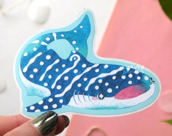 Op de afbeelding: Een blauwe en witte walvishaai sticker met een roze mond en witte stippen. De sticker is op een lichtroze achtergrond.