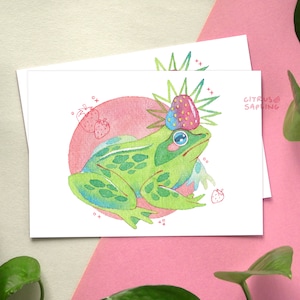 May include: A green frog with a pink strawberry crown sits on a pink and white background. The frog is surrounded by small pink strawberries.